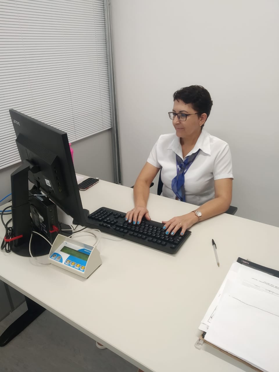 Mulher sentada olha para a tela do computador com suas mãos apoiadas no teclado da mesa.